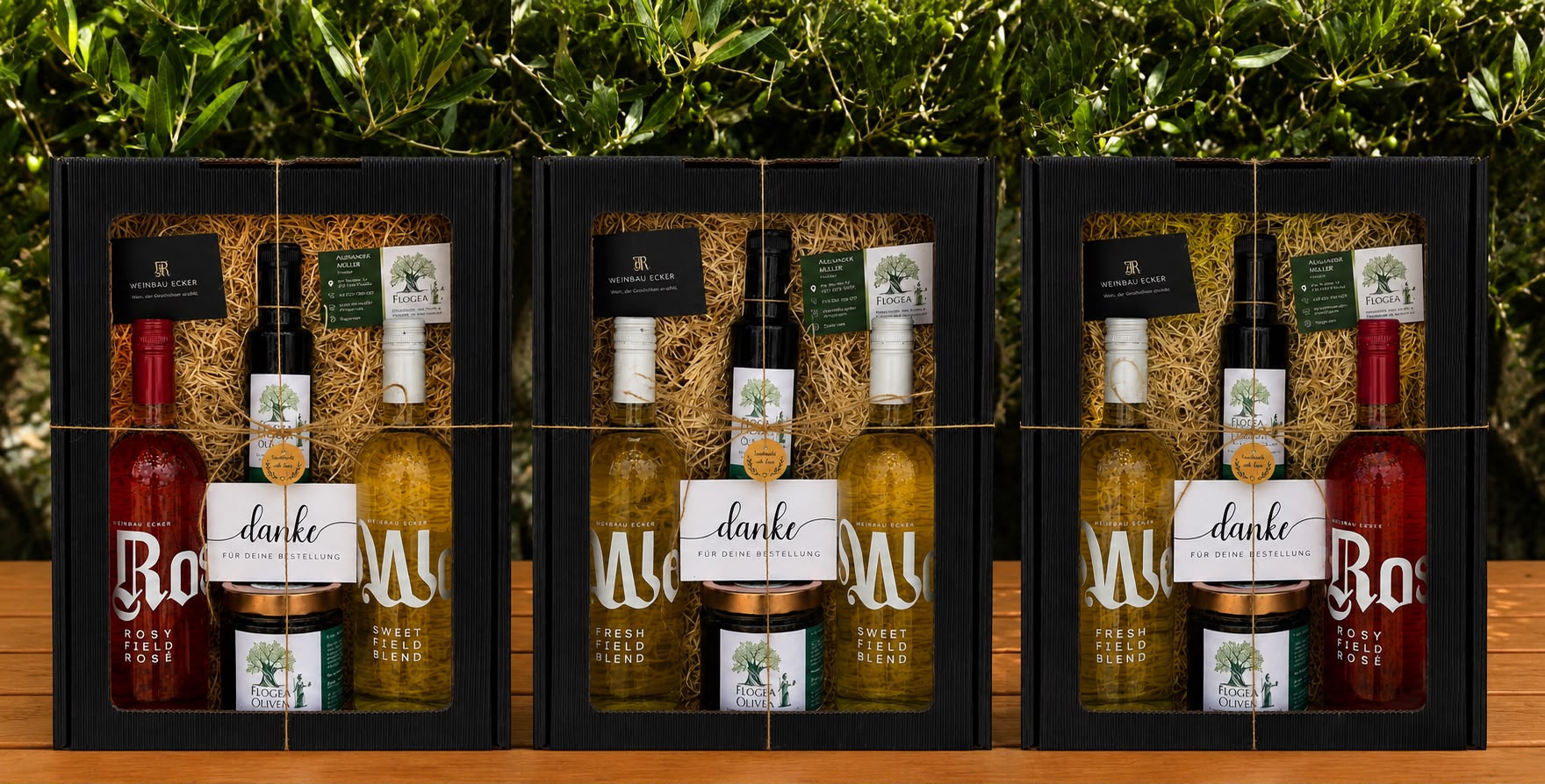 Drei Weinbau Ecker Geschenkboxen mit Wein und Olivenöl auf einem Holztisch